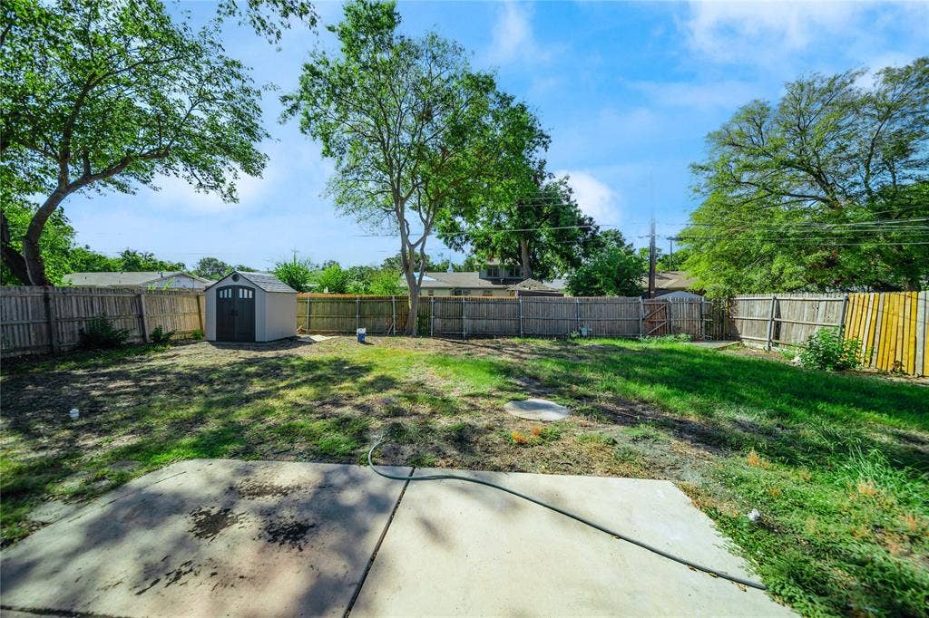 Spacious backyard featuring a concrete patio, perimeter wood fencing, and a detached storage shed