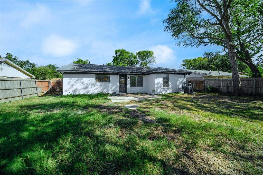 Rear exterior featuring a concrete patio, white stucco siding, and enclosed wood fencing with mature trees