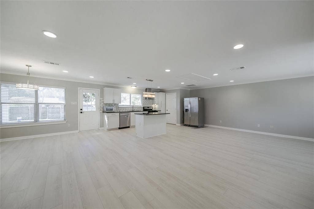 Open-concept interior featuring wood-finish flooring, recessed lighting, white cabinetry, a center kitchen island, and stainless steel appliances