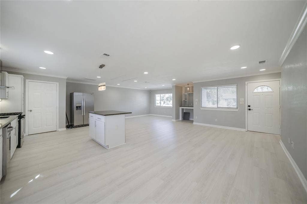 Open floor plan featuring wood-finish flooring, recessed lighting, a central kitchen island with a dark countertop, and a built-in dry bar