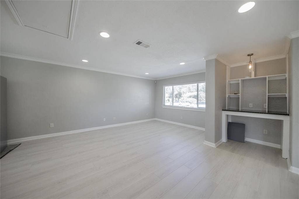 Neutral-toned interior featuring wood-finish flooring, recessed lighting, crown molding, and a built-in workstation with integrated shelving