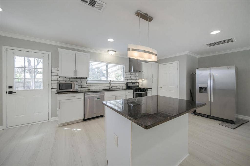 Kitchen featuring white cabinetry, stone-finish countertops, subway tile backsplash, a center island, and stainless steel appliances
