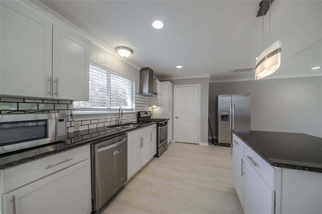 Kitchen featuring white shaker-style cabinetry, contrasting dark countertops, white subway tile backsplash, stainless steel appliances, and wood-finish flooring