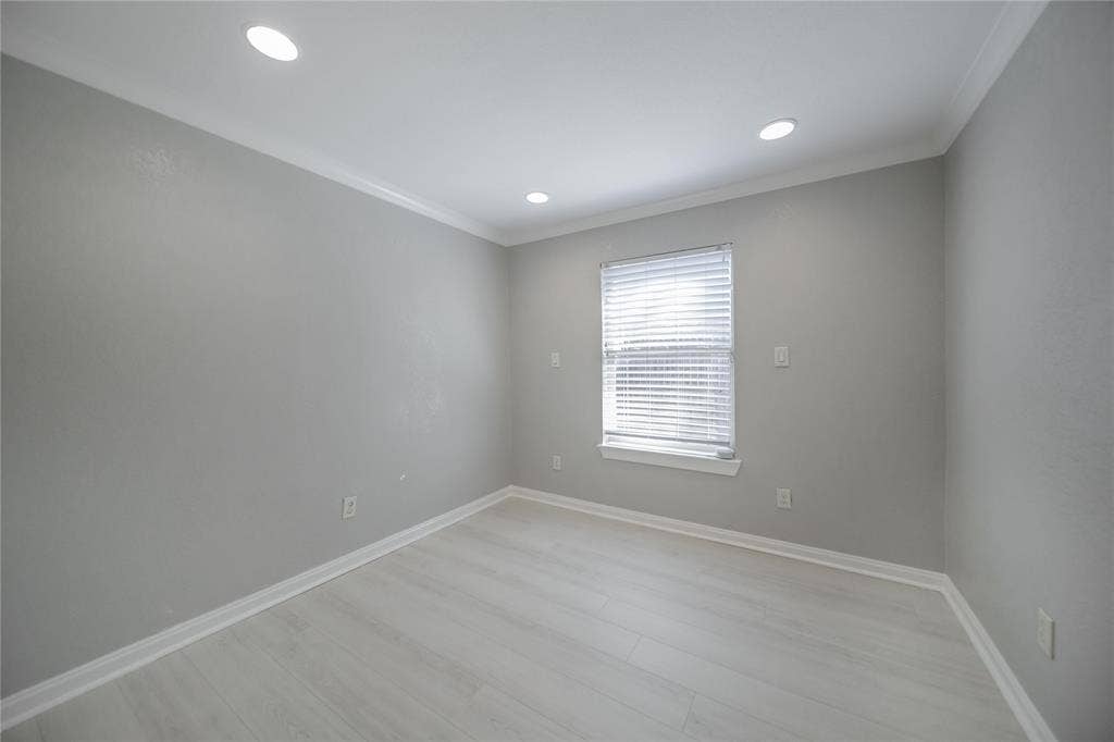 Neutral-toned interior space featuring light wood-finish flooring, recessed lighting, crown molding, and a single window with horizontal blinds