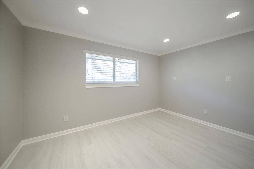 Neutral-toned interior featuring wood-finish flooring, recessed lighting, crown molding, and a horizontal window with attached blinds