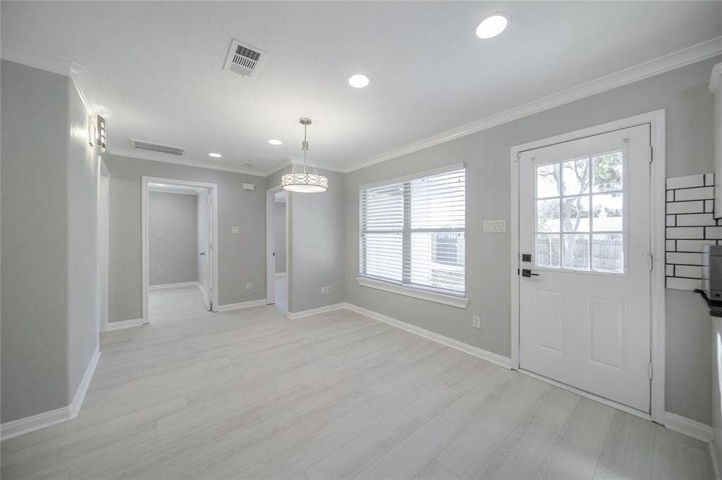 Neutral-toned interior featuring wood-finish flooring, recessed lighting, crown molding, a multi-pane glass entry door, and a drum-style pendant light fixture