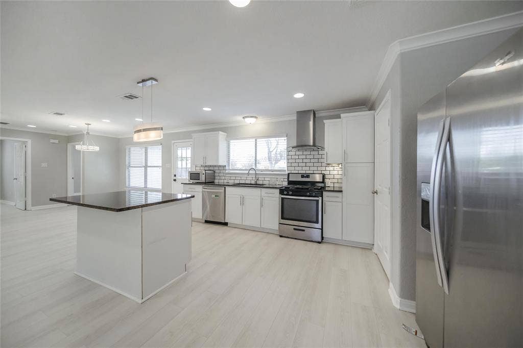 Kitchen featuring white shaker-style cabinetry, dark stone-finish island countertop, stainless steel appliances, subway tile backsplash, and wood-finish flooring