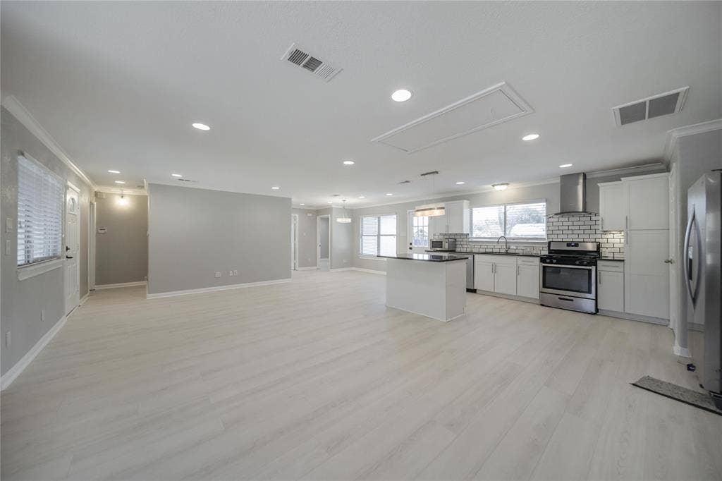 Open-concept kitchen and living area featuring wood-finish flooring, a central island, recessed lighting, and white cabinetry complemented by a white brick-pattern backsplash