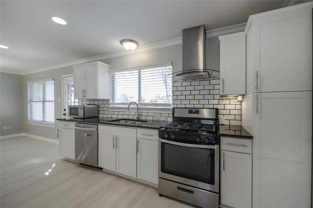 Kitchen featuring white Shaker-style cabinetry, dark countertops, subway tile backsplash, stainless steel appliances, and recessed lighting