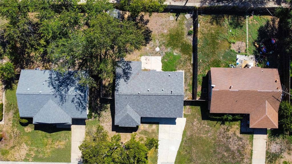 Aerial perspective of the property featuring a concrete driveway, multi-gabled shingle roofing, and expansive grounds with mature trees