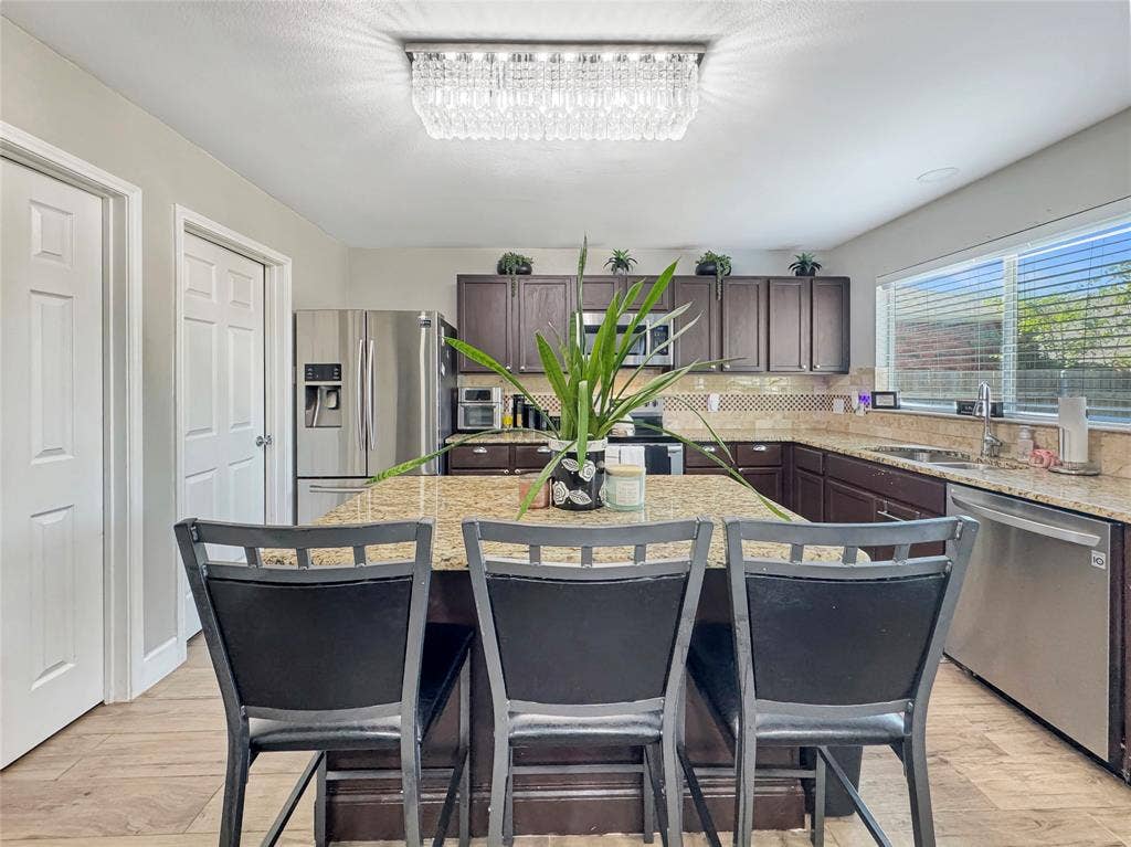 Kitchen featuring dark-finish cabinetry, stone-surface countertops, central island, stainless steel appliances, and rectangular crystal flush-mount lighting