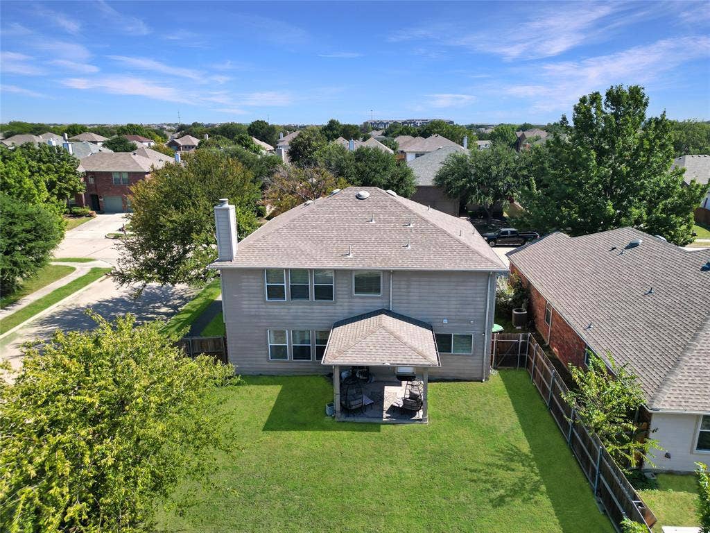 Two-story residence featuring a covered rear patio, expansive lawn, mature trees, and shingle roofing