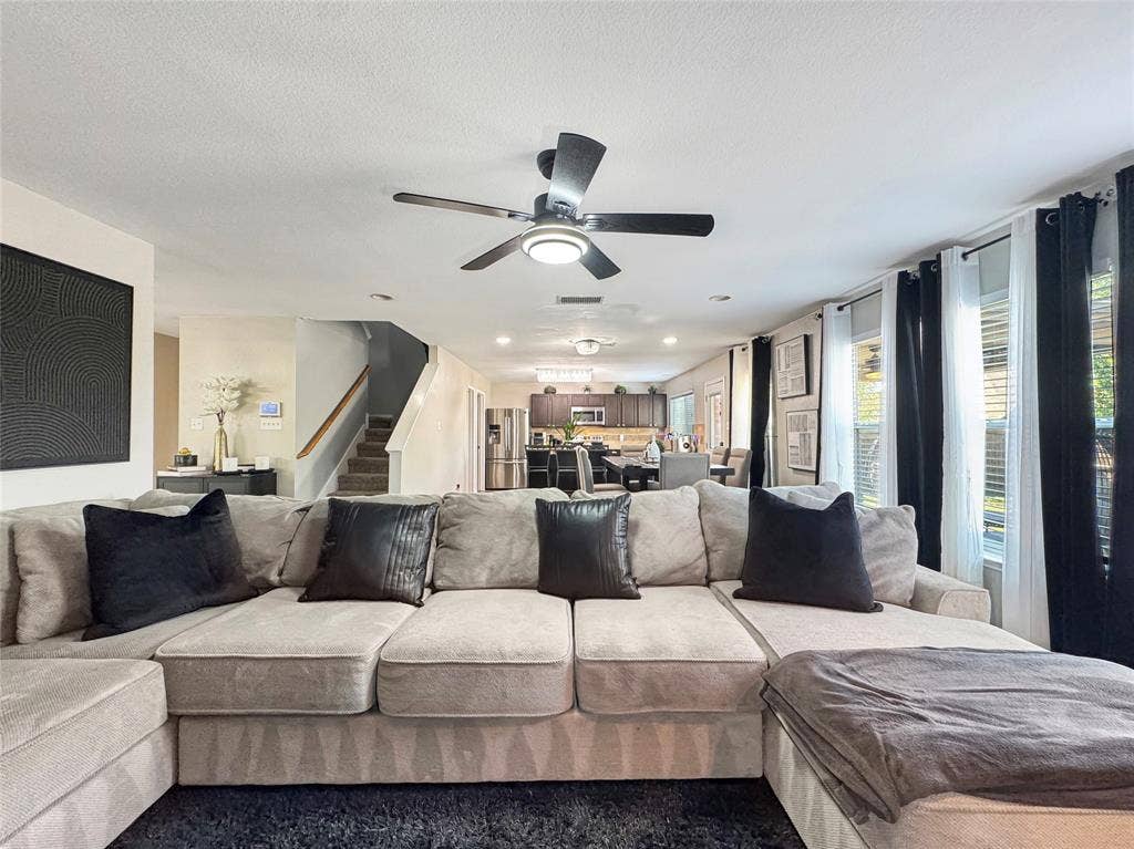 Open-concept interior featuring recessed lighting, a multi-blade ceiling fan, and a staircase with a wooden handrail