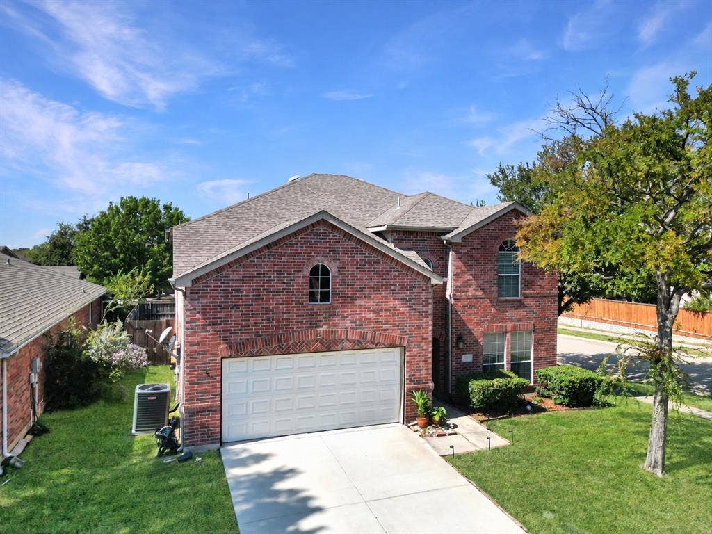 Brick exterior featuring an arched entryway, shingle roofing, multi-pane windows, and a double-car garage
