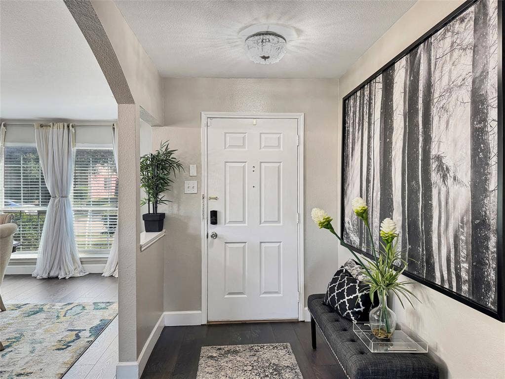 Foyer featuring dark wood-finish flooring, a flush-mount crystal-style light fixture, and an arched architectural opening