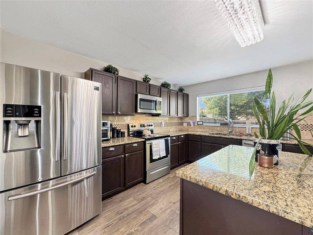 Kitchen featuring dark-finish cabinetry, stone countertops, stainless steel refrigerator, built-in microwave, and wood-finish flooring