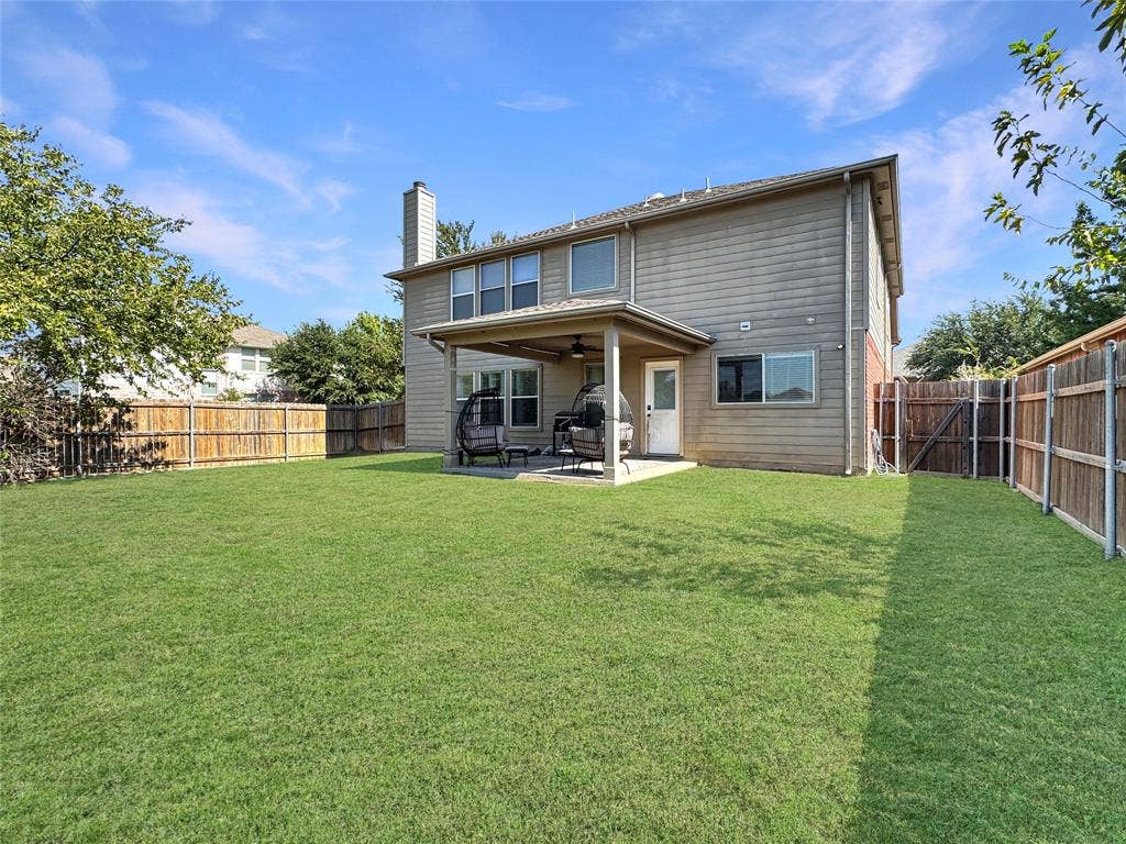 Expansive backyard featuring a manicured lawn, full wood privacy fencing, and a covered rear patio with a ceiling fan