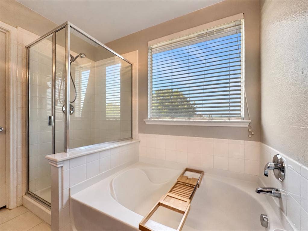 Glass-enclosed shower with chrome fixtures, deep soaking tub, and tile surround