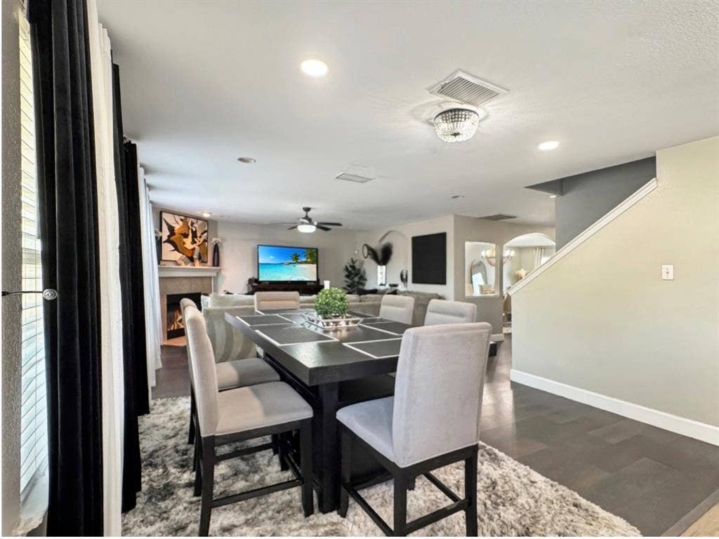 Open-concept living space featuring wood-finish flooring, a neutral color palette, recessed lighting, and a fireplace with a stone-finish surround