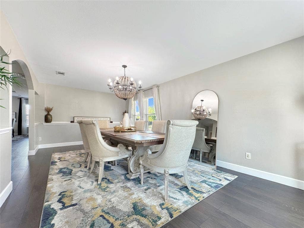 Dining area featuring dark wood-finish flooring, a spherical tiered chandelier, arched architectural detailing, and chair rail molding