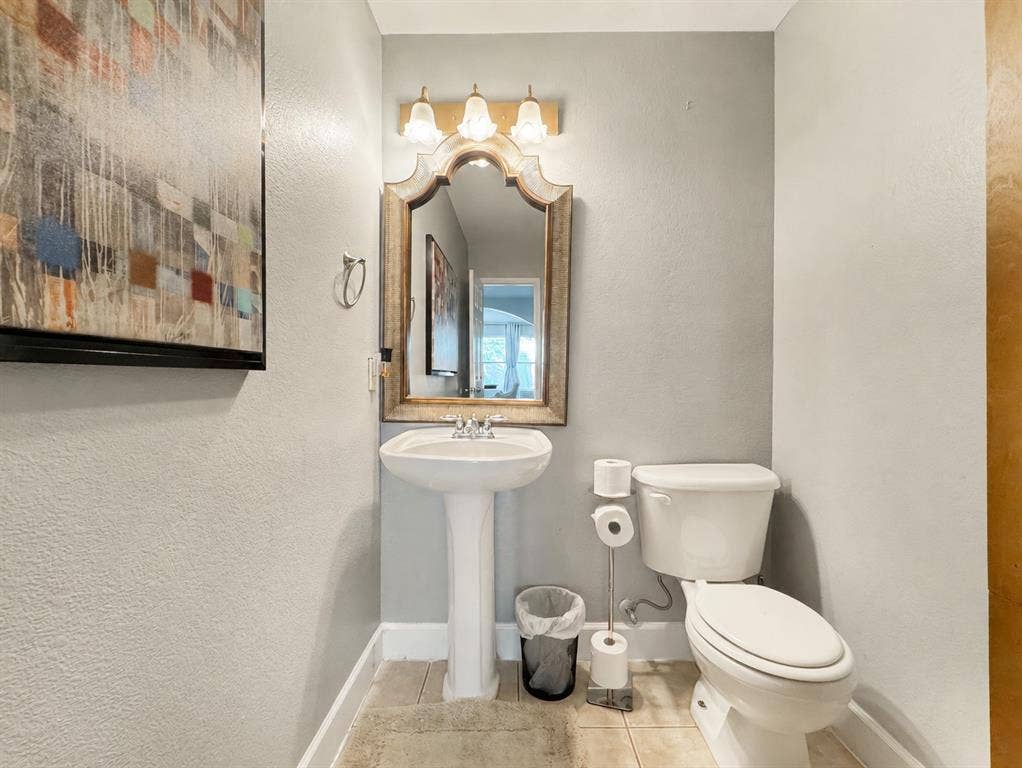 Powder room featuring a ceramic pedestal sink, arched wall-mounted mirror, three-light vanity fixture, and tiled flooring