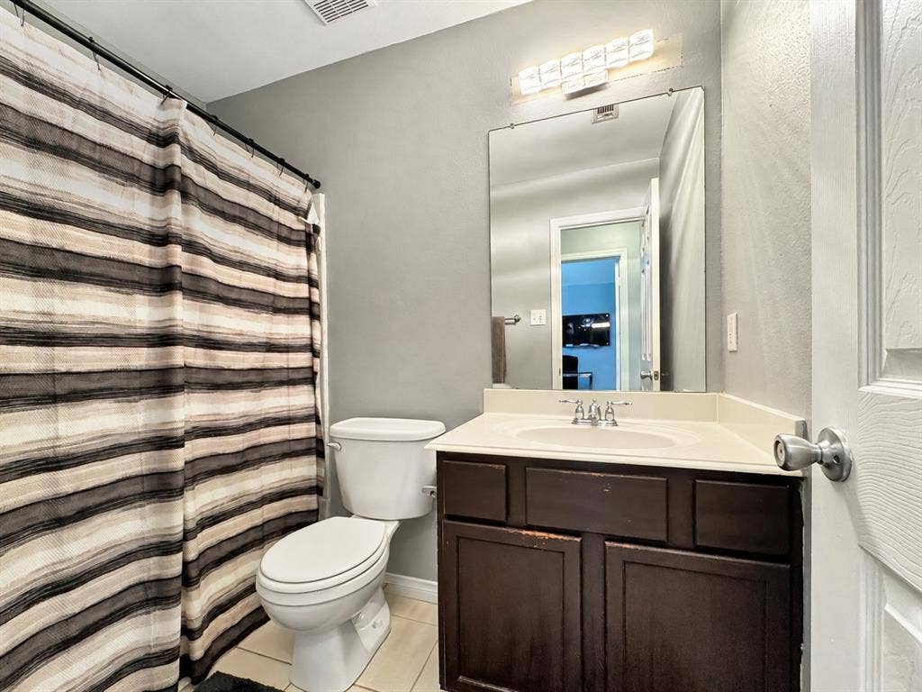Dark wood cabinetry, rectangular wall-mounted light fixture, large vanity mirror, molded sink basin, and tile flooring