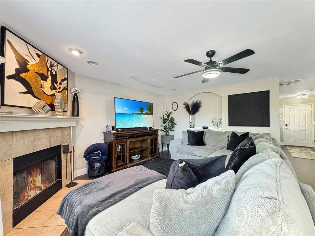Fireplace with a tile surround and mantel, recessed lighting, ceiling fan with integrated light fixture, and arched wall niche