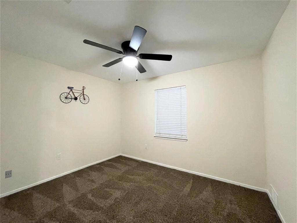 Neutral-toned room featuring wall-to-wall carpeting, a multi-blade ceiling fan with an integrated light fixture, and a window with horizontal blinds