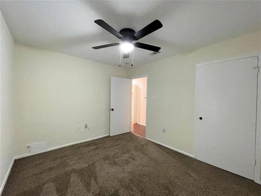 Neutral wall finish with carpeting and a matte black ceiling fan featuring an integrated light fixture, complemented by white interior doors