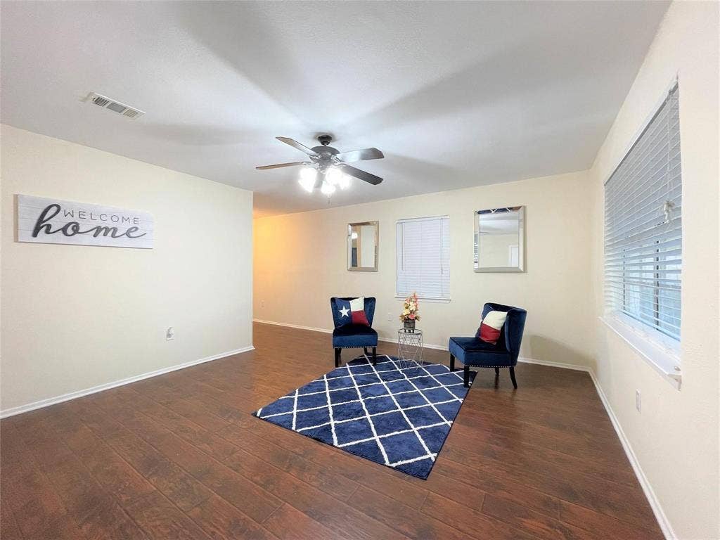 Living space featuring wood-finish flooring, a multi-blade ceiling fan with integrated lighting, and horizontal window blinds