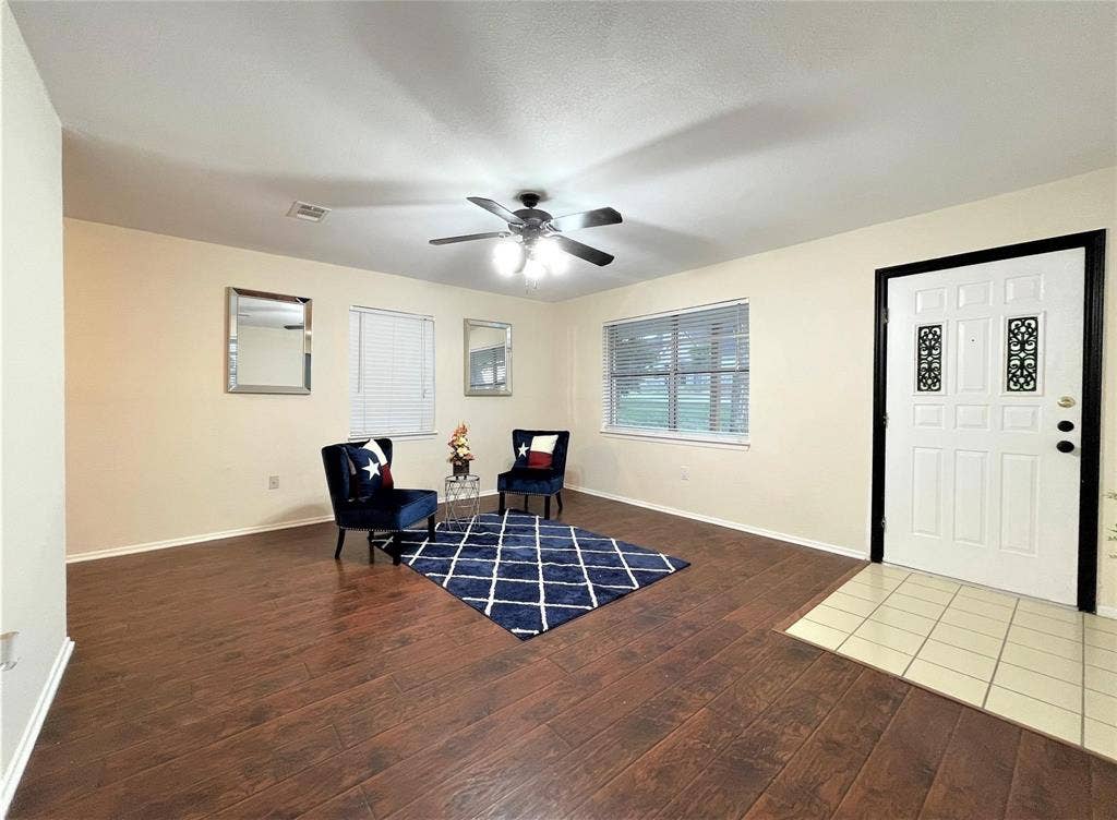 Living area featuring wood-finish flooring, neutral wall paint, a ceiling fan with integrated lighting, and a multi-panel door with decorative inserts