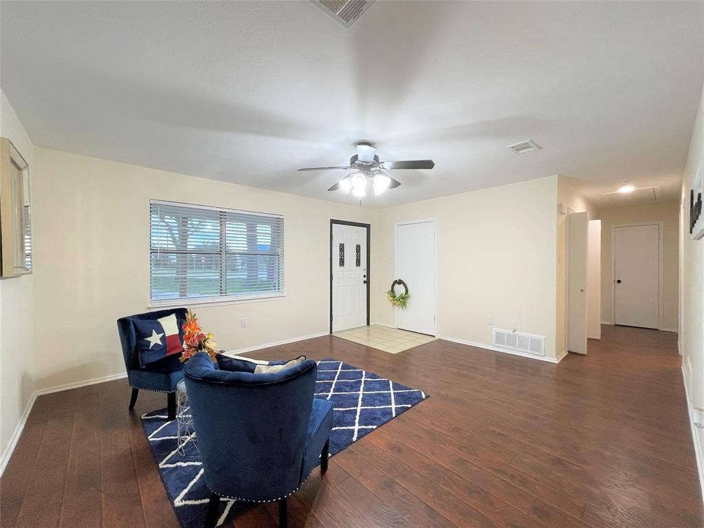 Living area featuring wood-finish flooring, vaulted ceiling, multi-blade ceiling fan with integrated lighting, and horizontal blind window treatment