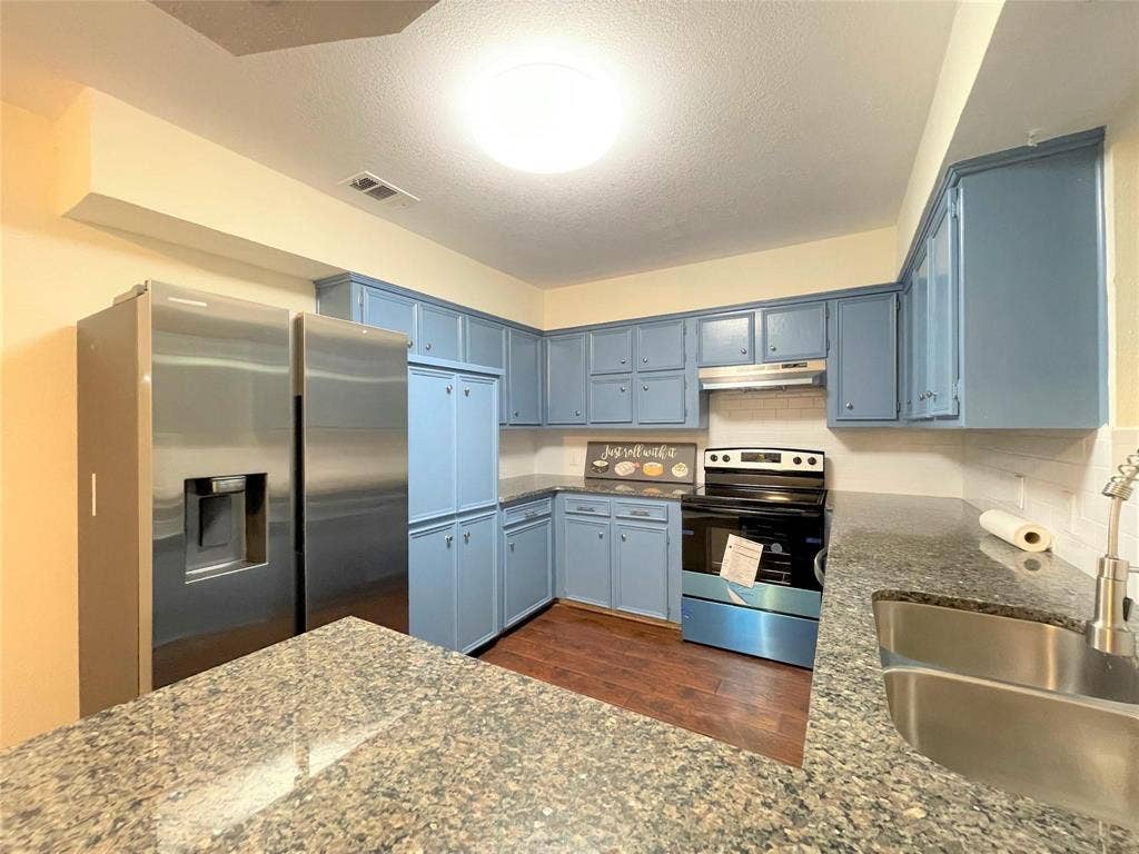 Kitchen featuring blue cabinetry, stone-finish countertops, stainless steel appliances, a double-basin undermount sink with a pull-down sprayer, and wood-finish flooring