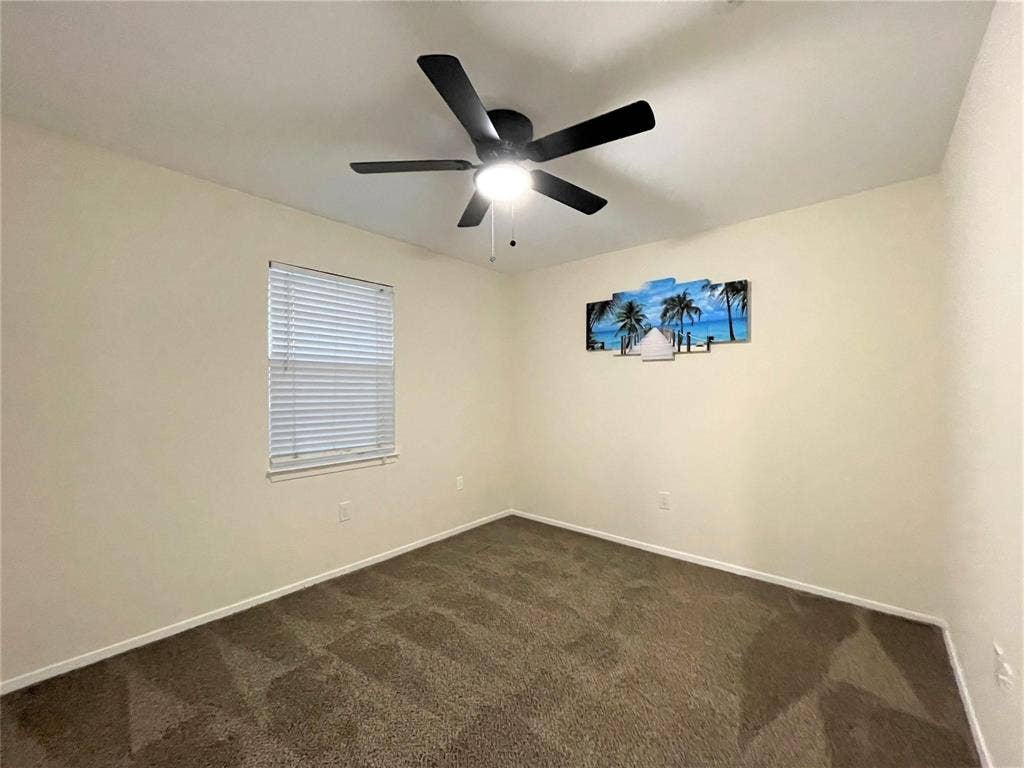 Neutral interior space featuring carpeted flooring, a ceiling fan with integrated lighting, and a window equipped with horizontal blinds