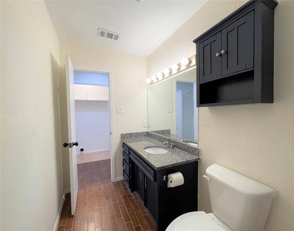 Bathroom featuring a stone-topped vanity with dark cabinetry, a wall-mounted medicine cabinet, a full-width vanity mirror with multi-bulb lighting, and tile flooring