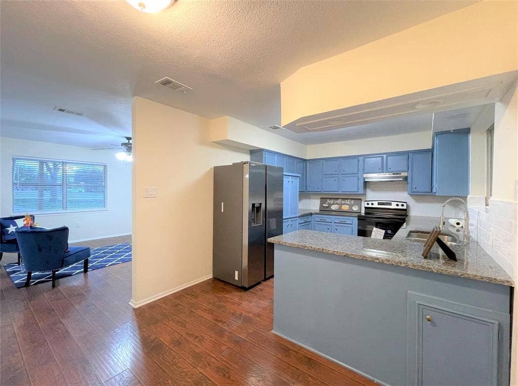Kitchen featuring a peninsula with stone-finish countertops, wood-finish flooring, stainless steel side-by-side refrigerator, and built-in blue cabinetry