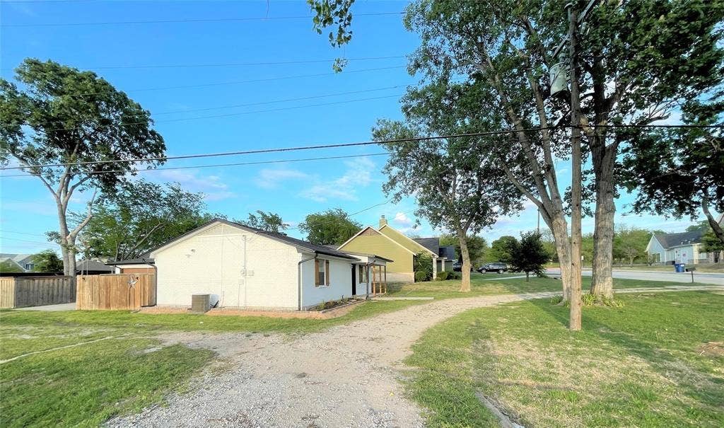 Stucco exterior, gravel driveway, wood-paneled privacy fencing, and mature trees on a level lot