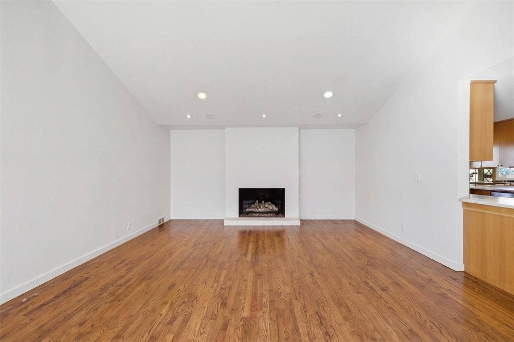 7606 Currin Drive, Dallas, TX 75230 Vaulted ceilings with recessed lighting, wood-finish flooring, and a central fireplace with a raised hearth