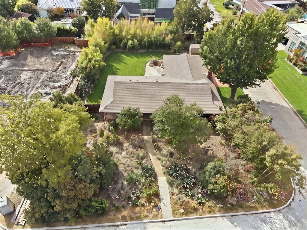 7606 Currin Drive, Dallas, TX 75230 Spacious corner lot featuring a maturely landscaped front yard with varied shrubbery, established trees, a paved walkway, a private rear lawn, and perimeter fencing
