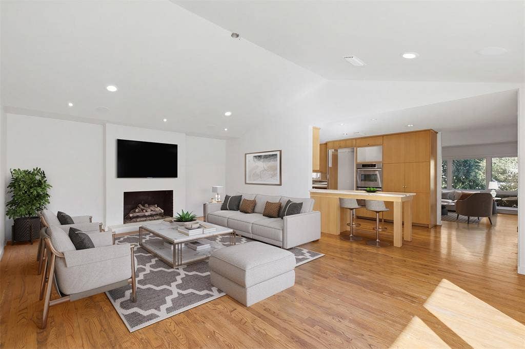 7606 Currin Drive, Dallas, TX 75230 Open-concept living space featuring wood-finish flooring, vaulted ceilings, recessed lighting, a fireplace with a minimalist hearth, and light-toned cabinetry with built-in appliances.