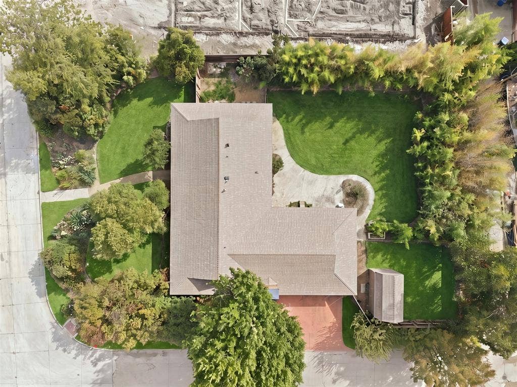 7606 Currin Drive, Dallas, TX 75230 Aerial perspective of a property featuring extensive green space, mature landscaping, a concrete patio, a dedicated storage structure, and a paved driveway