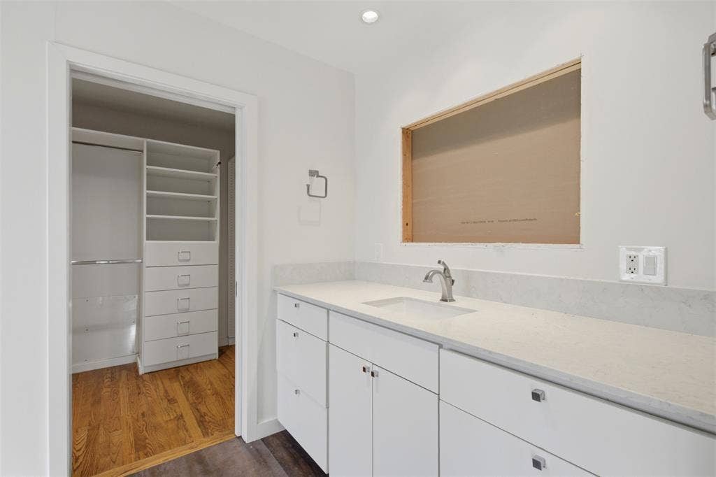 7606 Currin Drive, Dallas, TX 75230 White vanity featuring stone-surface countertop with undermount sink and matte hardware, complemented by custom built-in closet shelving and wood-finish flooring