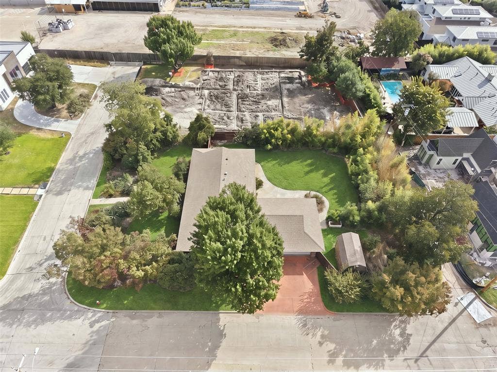 7606 Currin Drive, Dallas, TX 75230 Aerial view of a residential lot featuring a mature tree-lined perimeter, a manicured lawn, a paved driveway, and an exterior storage structure