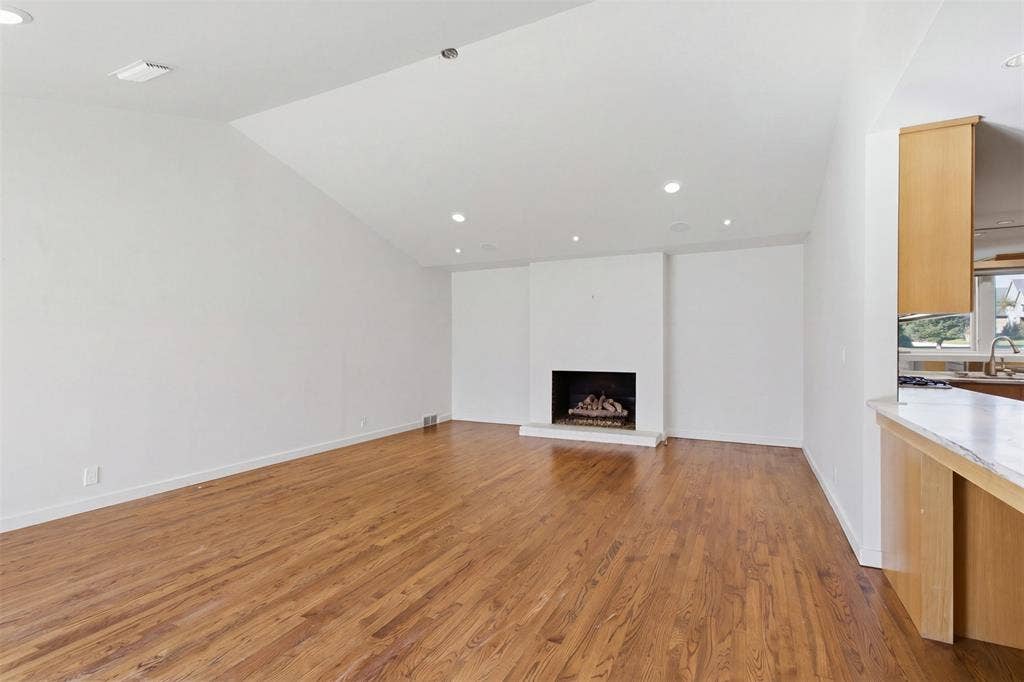 7606 Currin Drive, Dallas, TX 75230 Vaulted ceilings, wood-finish flooring, recessed lighting, and a prominent fireplace with a clean-lined mantel