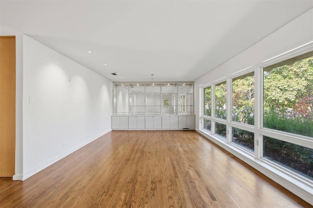 7606 Currin Drive, Dallas, TX 75230 Large living space featuring wood-finish flooring, a wall of floor-to-ceiling windows, recessed lighting, and built-in floor-to-ceiling shelving with glass cabinet fronts