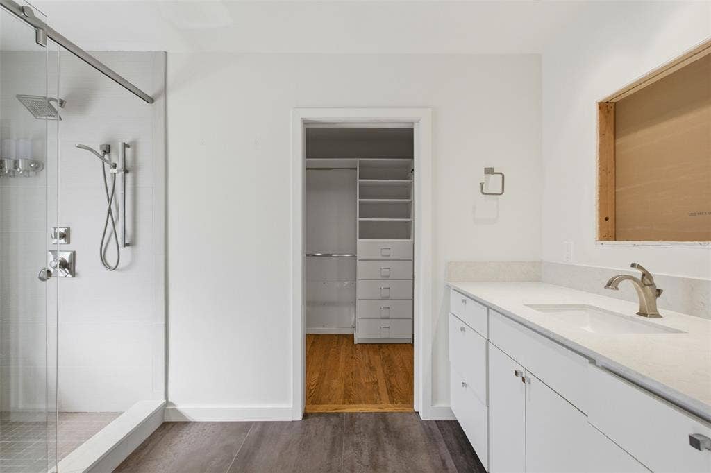 7606 Currin Drive, Dallas, TX 75230 Walk-in shower with glass enclosure and rainfall showerhead, vanity with stone-style countertop and undermount sink, and built-in closet organization system