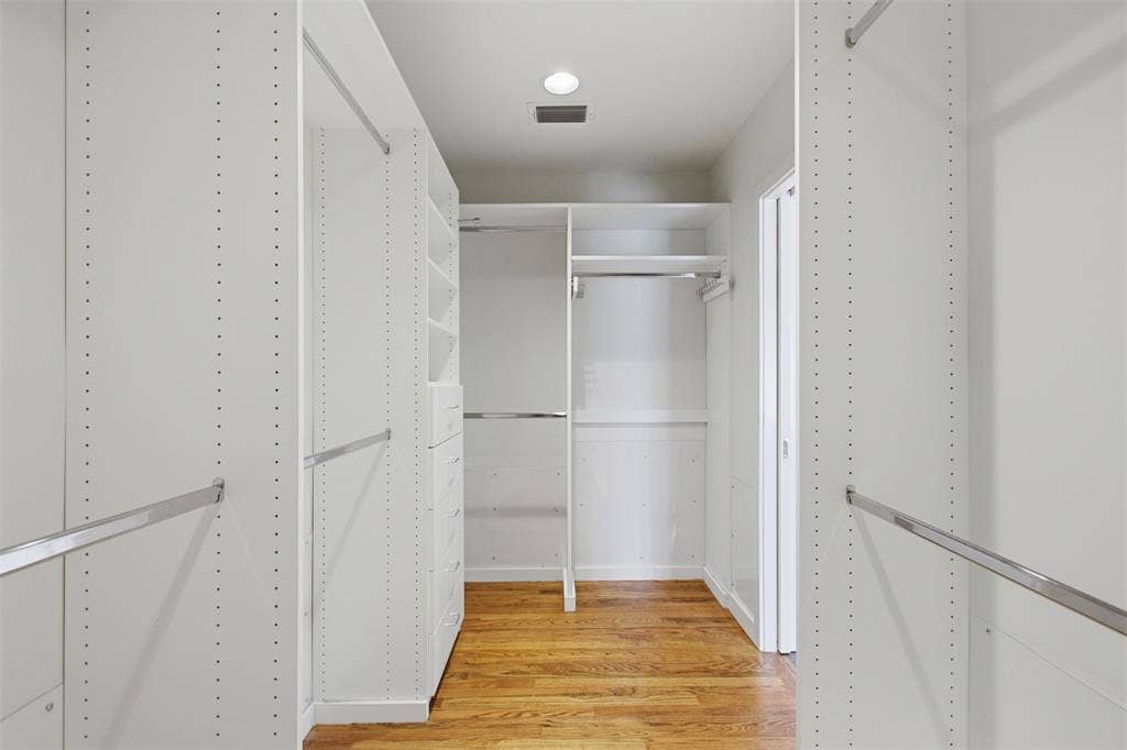 7606 Currin Drive, Dallas, TX 75230 Walk-in closet featuring white built-in shelving, integrated dresser drawers, chrome hanging rods, and wood-finish flooring