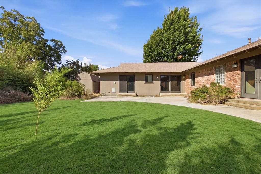 7606 Currin Drive, Dallas, TX 75230 Backyard featuring a concrete patio, exterior brick masonry, sliding glass doors, and a detached storage shed