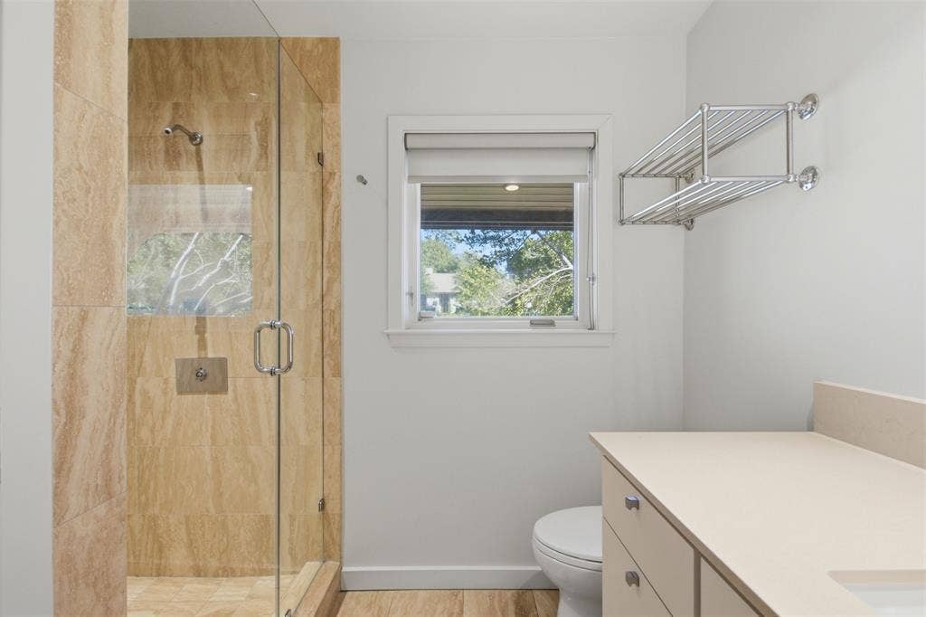 7606 Currin Drive, Dallas, TX 75230 Walk-in shower with stone-tile surround, glass enclosure, polished metal hardware, integrated vanity with composite countertop, and wall-mounted metal shelving