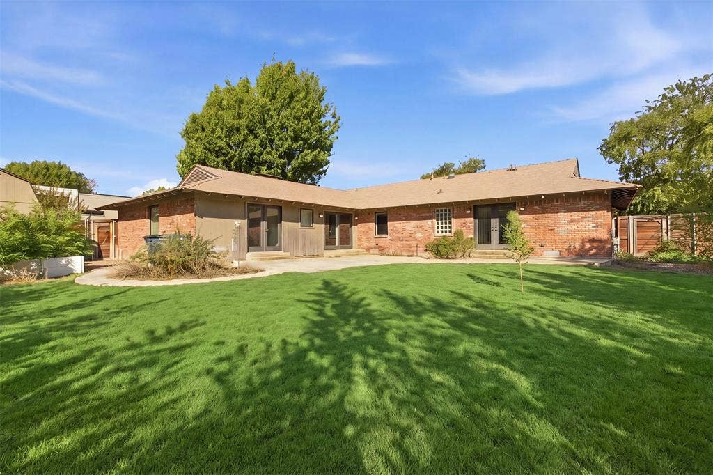 7606 Currin Drive, Dallas, TX 75230 Rear exterior featuring a brick facade, multi-pane French doors, concrete patio, and a manicured lawn